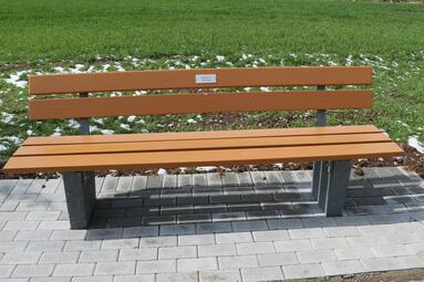 Vergrößerte Ansicht von Sitzbank mit Metallschild, auf dem Schild ist ein kurzer Text erkennbar