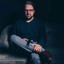 Vergrößerte Ansicht von Markus B. Altmeyer sitzt auf einem Sessel und hält einen übergroßen Bleistift in der Hand.