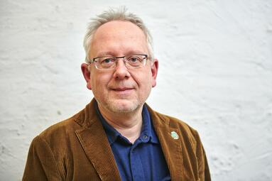 Vergrößerte Ansicht von Henner Kallmeyer, kurze graue Haare, brille, braune Jacke, von der Brust aufwärts fotographiert, lächelt in die Kamera.