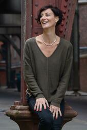 Vergrößerte Ansicht von Tania Witte lehnt an einer Säule und schaut lachend zur Seite.