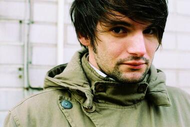 Vergrößerte Ansicht von Saša Stanišić trägt einen Parka, die Haare sind ihm übers linke Auge gefallen. Man sieht ihn von der Brust aufwärts.