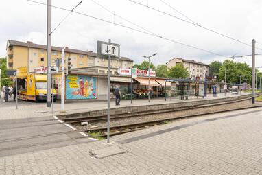 Vergrößerte Ansicht von Endhaltestelle mit wartenden Personen und Lebensmittelladen im Hintergrund