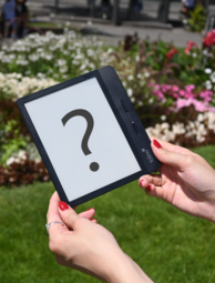 Vergrößerte Ansicht von Hände halten einen E-Book-Reader, auf dem ein großes Fragezeichen abgebildet ist.