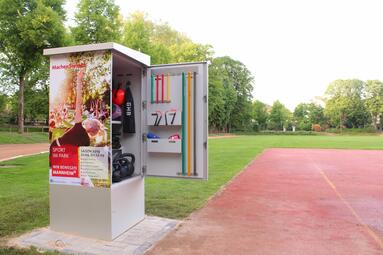 Vergrößerte Ansicht von Da sich Sportangebote im Freien einer steigenden Nachfrage erfreuen, hat die Stadt Mannheim 2019 im Unteren Luisenpark eine sogenannte „SportBox“ aufstellen lassen. Sportler*innen können sich hier Fitness-Equipment in der Nähe der Calisthenicsanlage ausleihen. Zum Inhalt dieser neuartigen „SportBox“ gehören klassische Ausrüstungen aus dem Functional Training wie TRX oder Kettlebells, Yogamatten, Kugelhanteln oder auch Gummibänder.