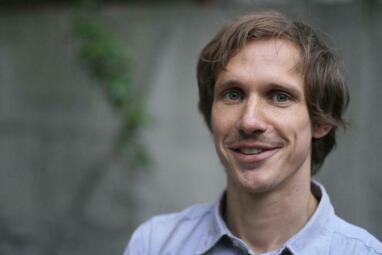 Vergrößerte Ansicht von Tobias Steinfeld im Portrait. Er hat etwas längere Haare, hat einen sympathischen Gesichtsausdruck und trägt ein blaues Hemd.