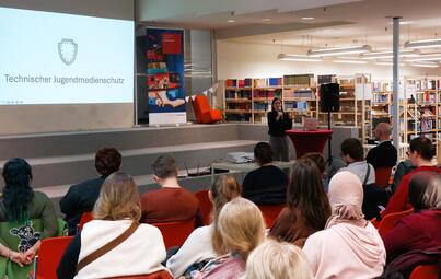 Vergrößerte Ansicht von Blick über die Schultern des Publikums auf die Referentin.