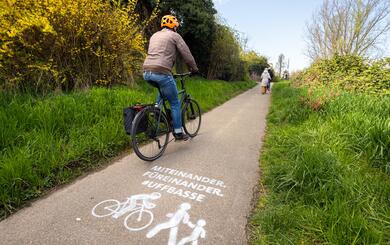 Fahrrad fährt auf Radweg. Kreidespray auf Fahrbahn weist auf ein rücksichtsvolles Miteinander hin