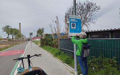 Person hängt Plakat der Aktion Rücksichtnahme auf Mannheims Fahrradstraßen am Rand einer Fahrradstraße auf