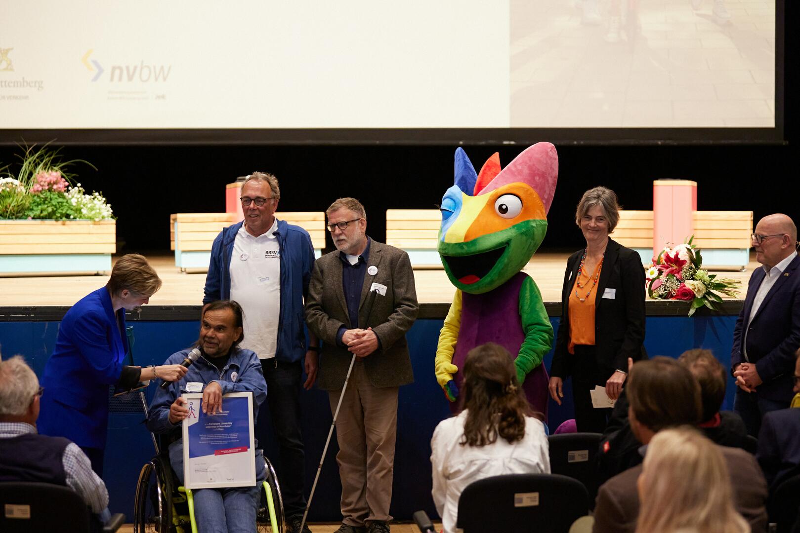 Heinrich Schaudt von der Arbeitsgemeinschaft Barrierefreiheit Rhein-Neckar e.V, Dr. Klaus Wolff und Karl-Heinz Schneider vom Badischen Blinden- und Sehbehindertenverein V.m.K. (BBSV), das Maskottchen Chämy, Ursula Frenz, Beauftragte für die Belange von Menschen mit Behinderungen der Stadt Mannheim und Verkehrsminister Winfried Hermann MdL bei der Preisverleihung