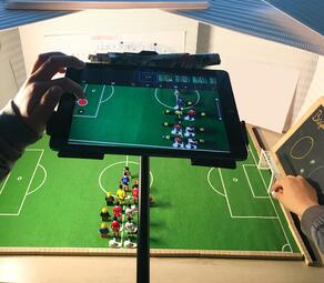 Vergrößerte Ansicht von Kinder erstellen am iPad einen Stop-Motion-Film über einem Miniatur-Fußballfeld