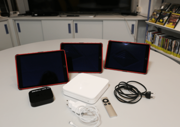 Vergrößerte Ansicht von Drei iPads, ein Apple TV, ein Airport und Kabel auf einem Tisch