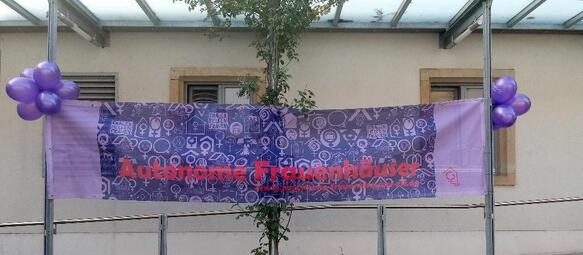 Vergrößerte Ansicht von Auf diesem Bild kann man eine lilane Flagge mit der Aufschrift &quot;Autonome Frauenhäuser&quot; sehen.