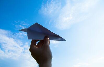 Vergrößerte Ansicht von Hand hält Papierflieger in blauen Himmel