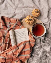 Vergrößerte Ansicht von Foto, auf dem unter anderem ein Buch, eine Tasse Tee und zwei kleine Kürbisse auf einem Bett drapiert sind