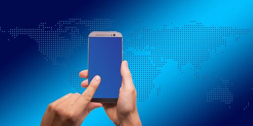 Vergrößerte Ansicht von Smartphone, gehalten vor blauer Weltkarte