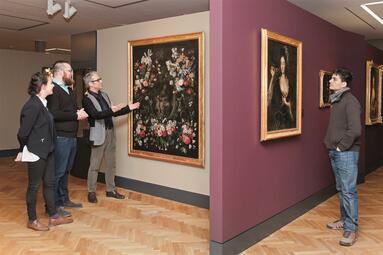 Vergrößerte Ansicht von Drei Männer und eine Frau betrachten in einer Ausstellung zwei große Gemälde mit Blumenmustern