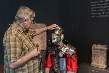 Vergrößerte Ansicht von Ein Mann ertastet den Helm einer Figurine mit römischer Legionäruniform