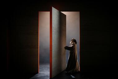 Vergrößerte Ansicht von Orsino tritt durch eine große Tür in der Holzwand. Das Licht lässt harte Schatten entstehen.