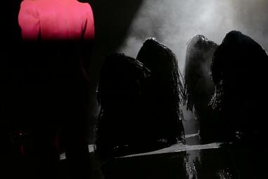 Vergrößerte Ansicht von Vier schwarze Gestalten bewegen sich vorgebeugt zum Bühnenrand.