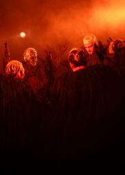 Vergrößerte Ansicht von rote Bühnenbeleuchtung. bDie schwarzen Gestalten stehen im Kreis und heben ihre Arme hoch.