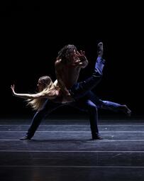 Vergrößerte Ansicht von Ein Tänzer balanciert eine Tänzerin auf seinem Knie. Es entsteht ein schwebend leichter Moment. Dunkle Lichtstimmung.