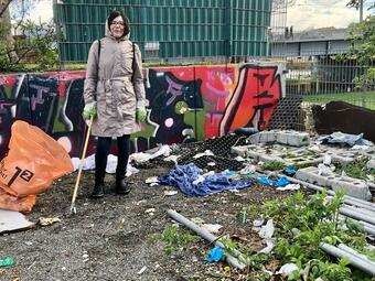 Vergrößerte Ansicht von Eine Frau steht auf dem Platz &quot;ALTER&quot; inmitten von Abfällen, die auf dem Boden liegen.