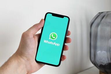 Vergrößerte Ansicht von Eine Hand hält ein Smartphone. Auf diesem ist ein WhatsApp-Symbol.