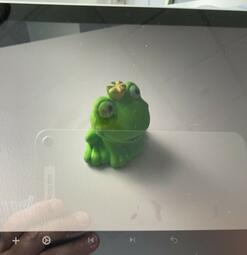Vergrößerte Ansicht von Ein Screenshot einer Froschkönig-Figur. In dem Bild spiegelt sich eine Hand, die ein Tablet hält.