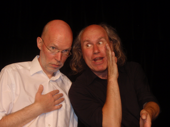 Vergrößerte Ansicht von Bei einem Auftritt lehnt sich einer der beiden Zweifler-Kabarettisten zum anderen rüber und flüstert ihm hinter vorgehaltener Hand etwas zu.