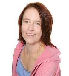 Vergrößerte Ansicht von Rike Reiniger vor weißem Hintergrund leicht nach vorn gebeugt, lächelt in die Kamera.