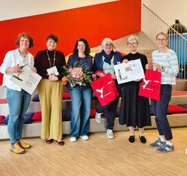 Vergrößerte Ansicht von Sechs Frauen stehen vor der roten Wand an der Lesetreppe im Biblabor und lächeln in die Kamera.