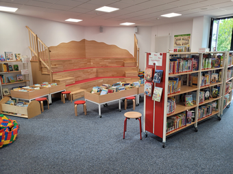 Vergrößerte Ansicht von Ein heller Bereich für Kinder in der Zweigstelle Schönau: mit Lesetreppe, niedrigen Bildberuchkisten und kindergerechten Büchern in Regalen.