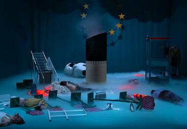 Vergrößerte Ansicht von Das Bühnenbild wird in dramatisches, dunkelblaues Licht getaucht. Der Boden ist vernebelt. 2D-Rosen, Schiffsgeländer und Schuhe liegen überall verstreut. Eine Telefonzelle, eine umgefallene Leiter und das Auspuffrohr eines Schiffes ragen aus dem…