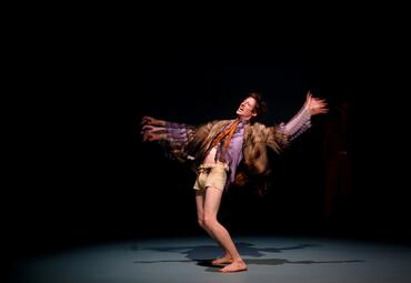 Vergrößerte Ansicht von Dramatisches Licht fällt auf eine Person in einer verbrannten Jacke und verbrannten Hemd. Die Person hat den Oberkörper zurückgelehnt, die Arme in einer wirbelnden Bewegung und das Gesicht vor Schmerzen verzerrt.Durch die schnelle Bewegung sind die…