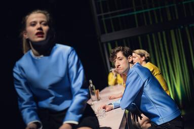 Vergrößerte Ansicht von Camille Dombrowsky (Nora) sitzt im Vordergrund auf einem Tisch, Rocco Brück (Helge) und Robin Krakowski (Tom)sitzen an ihm.