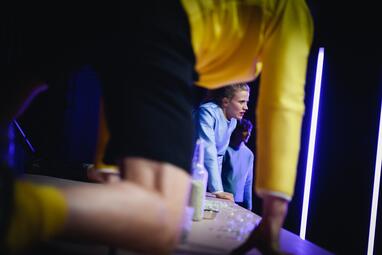 Vergrößerte Ansicht von Robin Krakowski (Tom) und Camille Dombrowsky (Nora) knien auf dem Tisch, Rocco Brück (Helge) steht im Hintergrund.