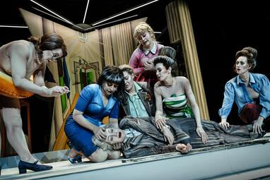 Vergrößerte Ansicht von Sechs Frauen, in unterschiedlichen Kleidungsstilen, trösten eine siebte Frau, in einem grauen Anzug, die weinend auf dem Boden liegt.