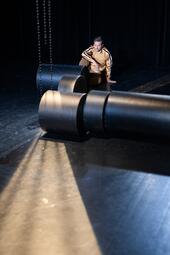 Vergrößerte Ansicht von Person in einem beigen Sportanzug kniet auf dem Boden und blickt auf zwei große schwarze Rollen