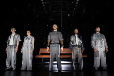 Vergrößerte Ansicht von Frontalaufnahme von fünf Personen in grauen, sportlichen Anzügen, starren in die Ferne. Sie sind alle in kaltes, weißes Licht getaucht.