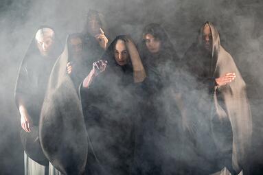 Vergrößerte Ansicht von Sechs Personen in schwarzen Kapuzen im Nebel