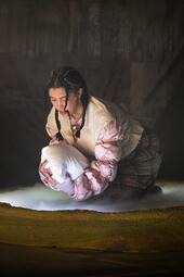 Vergrößerte Ansicht von Frau kniet im Nebel und hält ein weißes Kissen wie ein Baby.