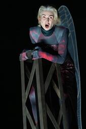 Vergrößerte Ansicht von Person in schwarz-rot mit roten Augen klammert sich singend an ein metallenes Gestell.