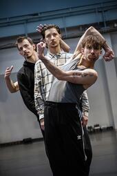 Vergrößerte Ansicht von Auf dem Bild sind vier Personen zu sehen, die hintereinander stehen. Die vorderste Person hat sich zur Seite gelehnt, die Arme angewinkelt und die Hände zu Fäusten geballt. Die andere Person steht aufrecht und die Arme sind am Körper angelegt, Die…