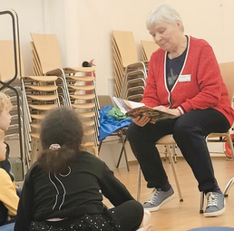 Vergrößerte Ansicht von Eine ältere Frau liest Kindern aus einem Buch vor. 