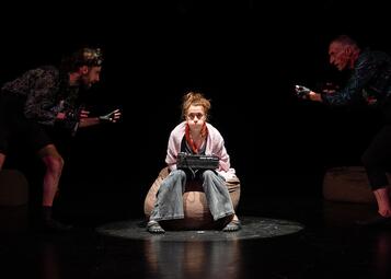 Vergrößerte Ansicht von Carmen Ipek sitzt mit aufgeblasenen Backen und einem Akai-MIDI Keyboard auf einem braunen Sack. Rechts und links von ihr Moritz Andrea Bürge und Uwe Topmann, die sie anzufeuern scheinen.