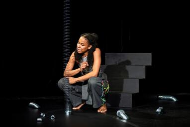 Vergrößerte Ansicht von Vor einer schwarzen Treppe geht eine Frau in die Hocke und schaut eine aufgespannte silberne Spirale vor sich an. Um sie herum liegen noch weitere silberne Spiralen verschiedener Größen herum.