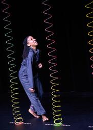 Vergrößerte Ansicht von Eine Frau steht seitlich zur Kameraund schaut lächelnd die rosa-gelbe Spirale vor sich an. Es sind noch zwei weitere Spiralen Richtung Decke aufgespannt.