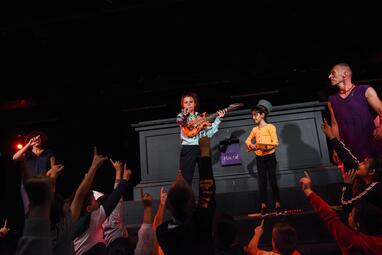 Vergrößerte Ansicht von Katharina Wawrik mit Luftgitarre, neben ihr ein Mädchen mit Hut und Holzflinte