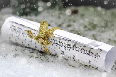 Vergrößerte Ansicht von Ein eingerolltes Blatt mit Musiknoten auf Schnee. Die Rolle ist mit gold-glitzerndem Band verschnürt.