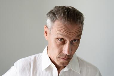 Vergrößerte Ansicht von Portrait von Farin Urlaub, mit weißem Hemd, gräulichen Haaren und strengem Blick mit hochgezogenen Augenbrauen.